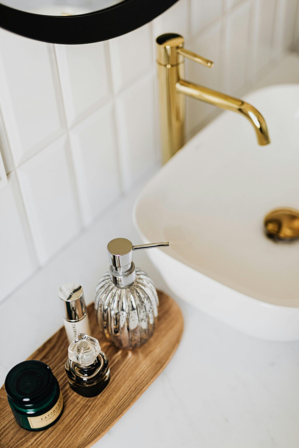 A stylish modern bathroom setup featuring a gold faucet, sink, and skincare products on a wooden tray.